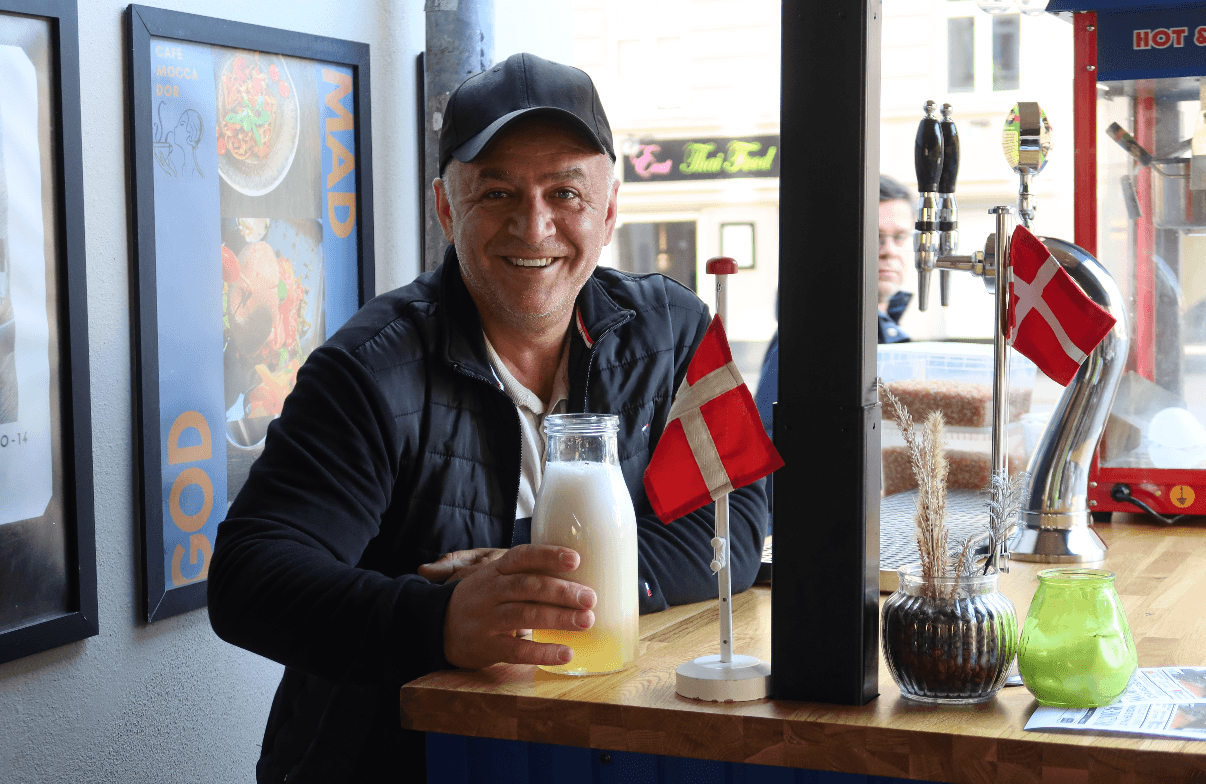 Ejeren af Café Moccador smilende bag baren med dansk flag