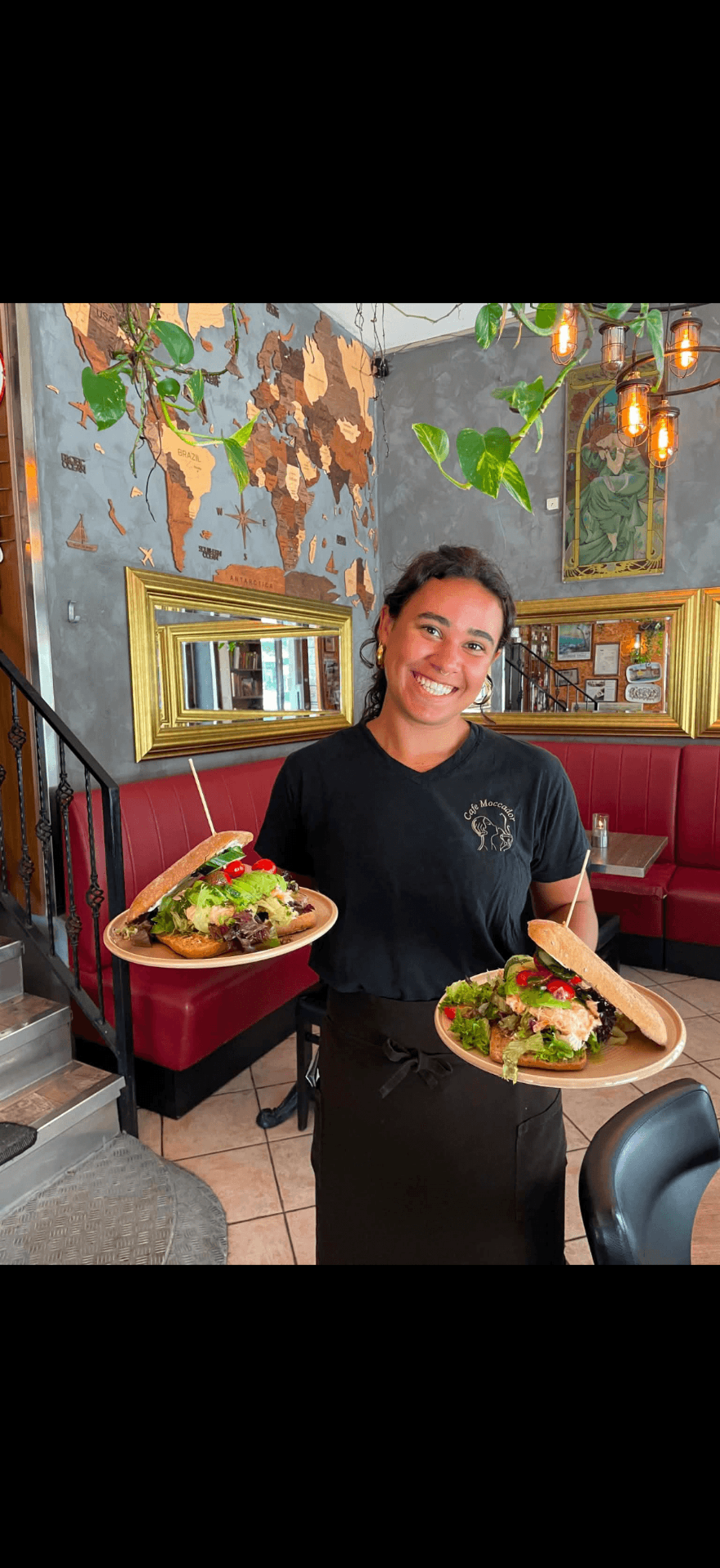 Smilende tjener med forklæde og bakke bag baren på Café Moccador